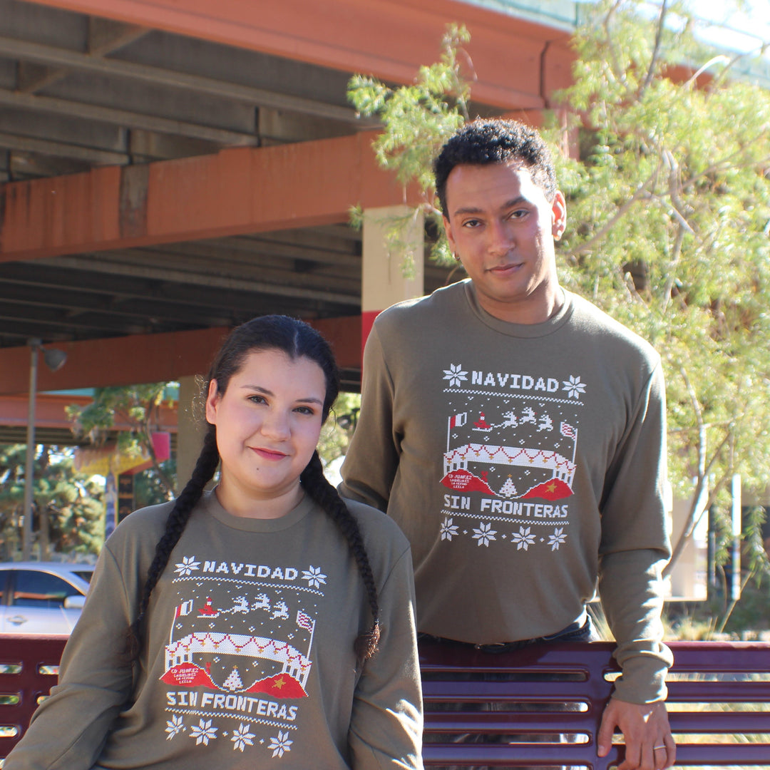 Two people wearing Navidad-themed sweatshirts sitting on a bench outdoors.