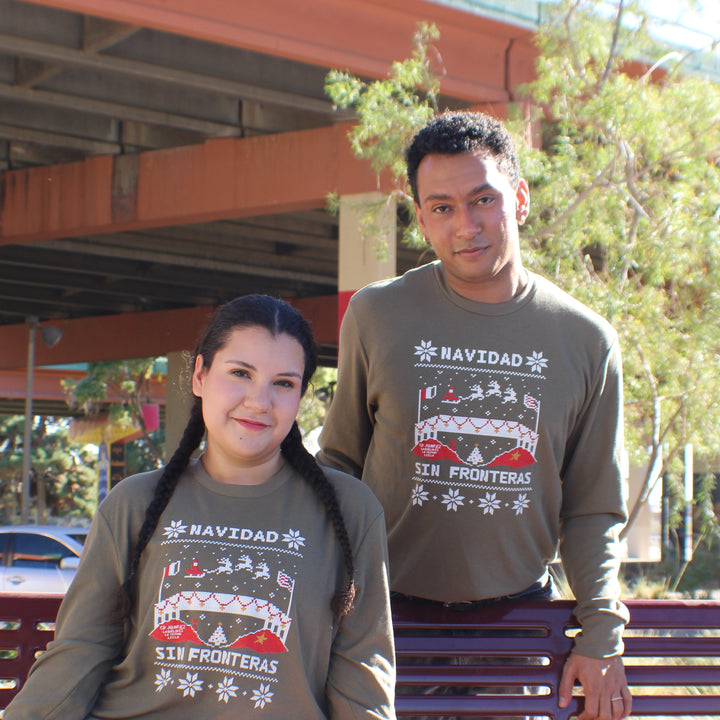 Two people wearing Navidad-themed sweatshirts sitting on a bench outdoors.